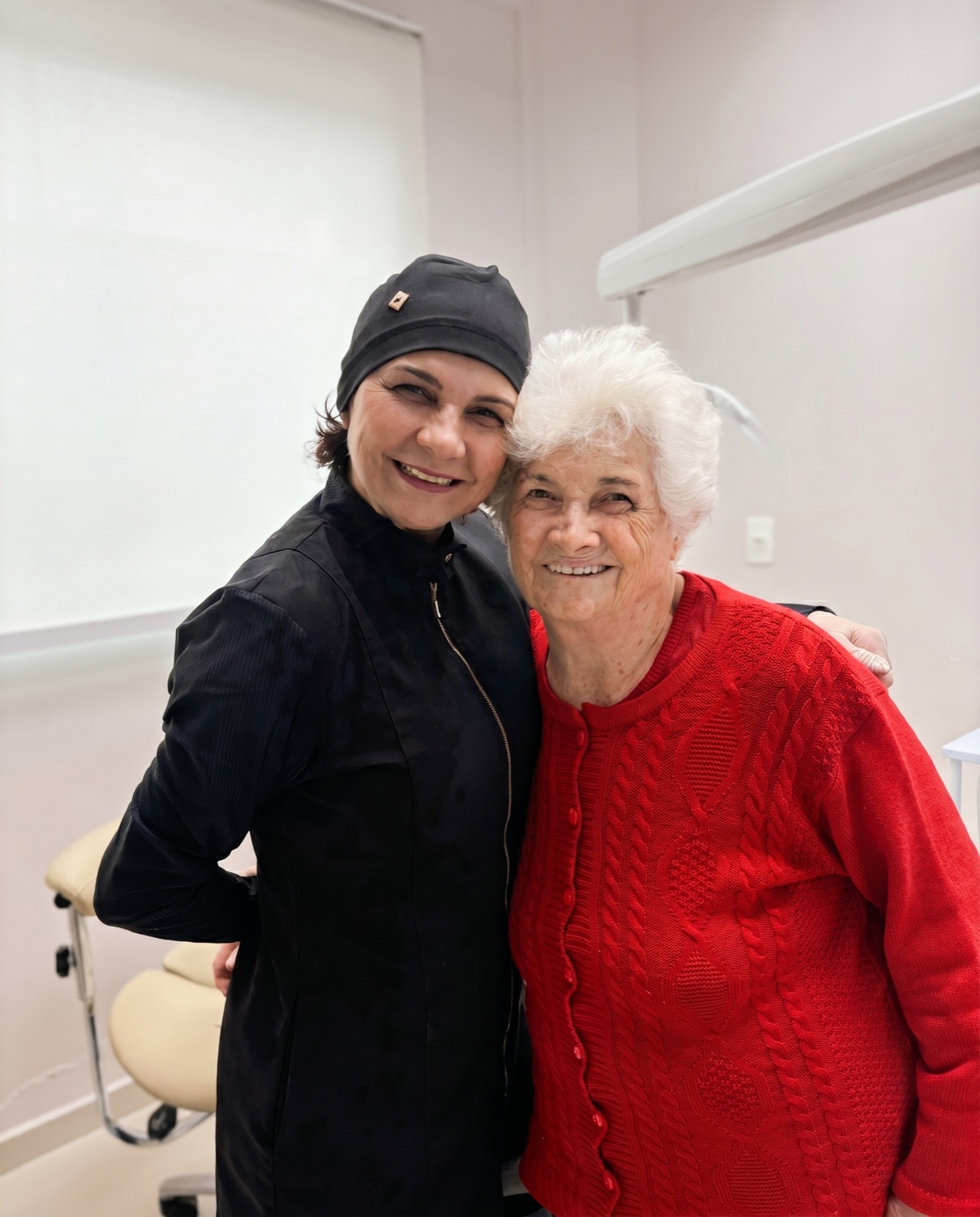 Dra. Ana Scatolin sorrindo, em um abraço acolhedor no consultório