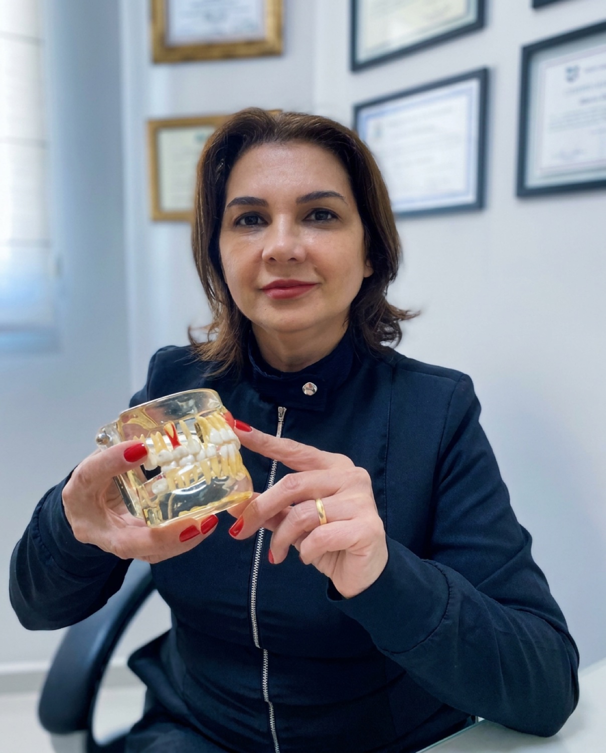 Dra. Ana Scatolin no consultório, segurando um modelo de implante dentário